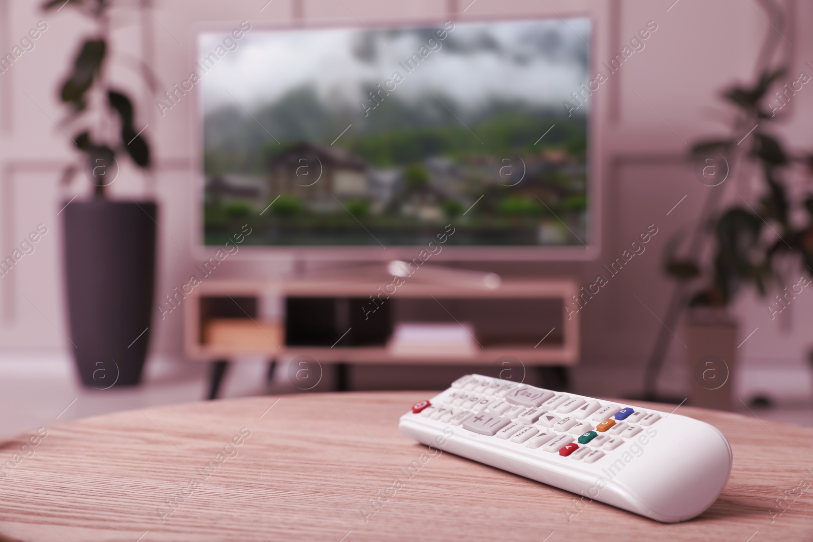 Image of Remote control on wooden table and TV screen in room, selective focus