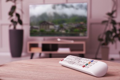 Remote control on wooden table and TV screen in room, selective focus