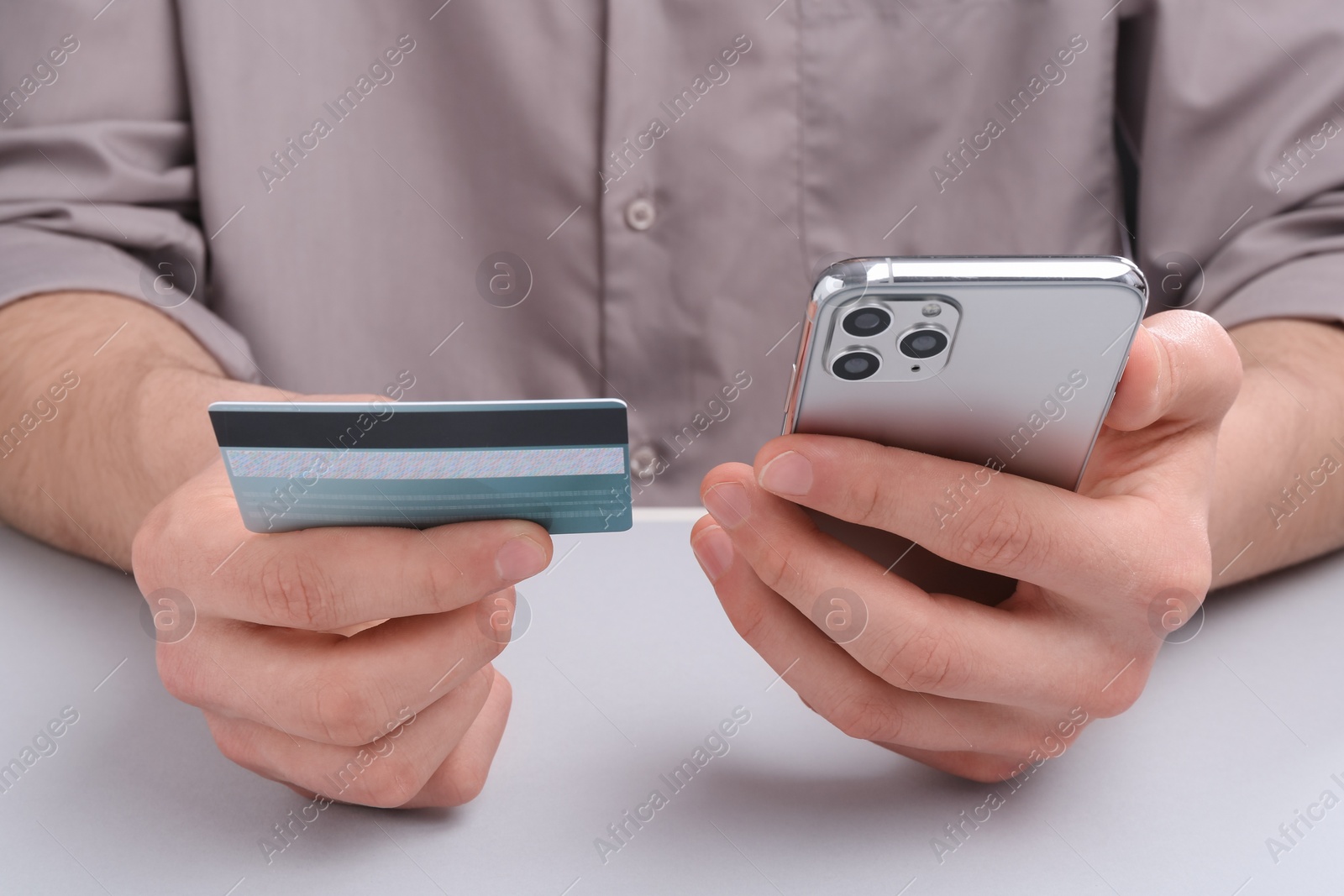 Photo of Online payment. Man with smartphone and credit card at light grey table, closeup