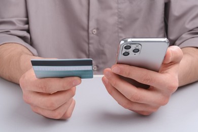 Online payment. Man with smartphone and credit card at light grey table, closeup