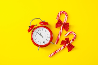 Alarm clock and candy canes on yellow background, flat lay. New Year countdown