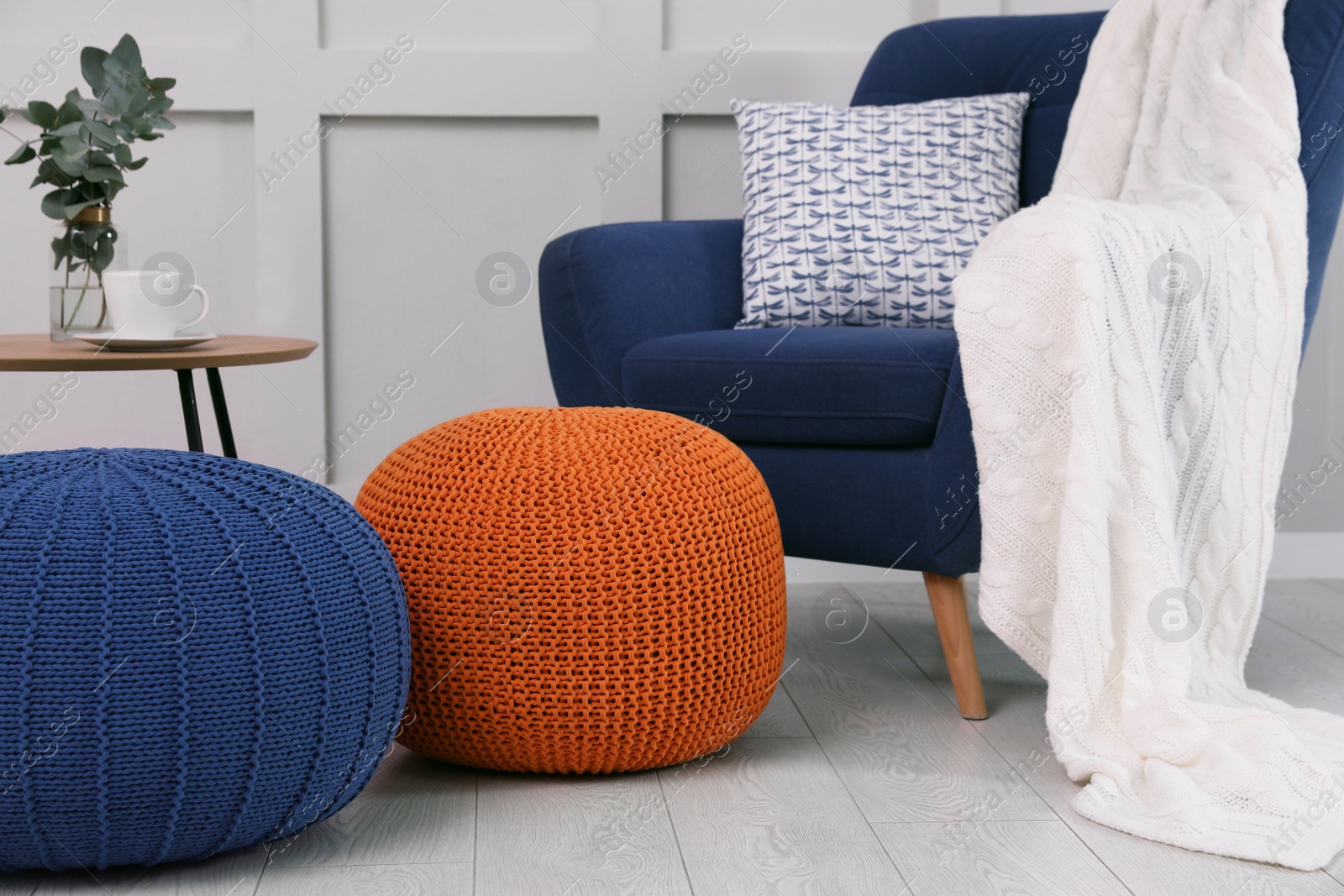 Photo of Stylish knitted poufs near armchair in room. Interior design