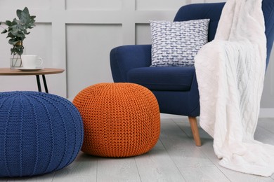 Photo of Stylish knitted poufs near armchair in room. Interior design