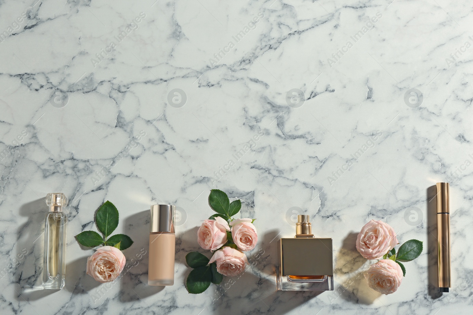 Photo of Flat lay composition with bottles of perfume, cosmetics and roses on marble background, space for text