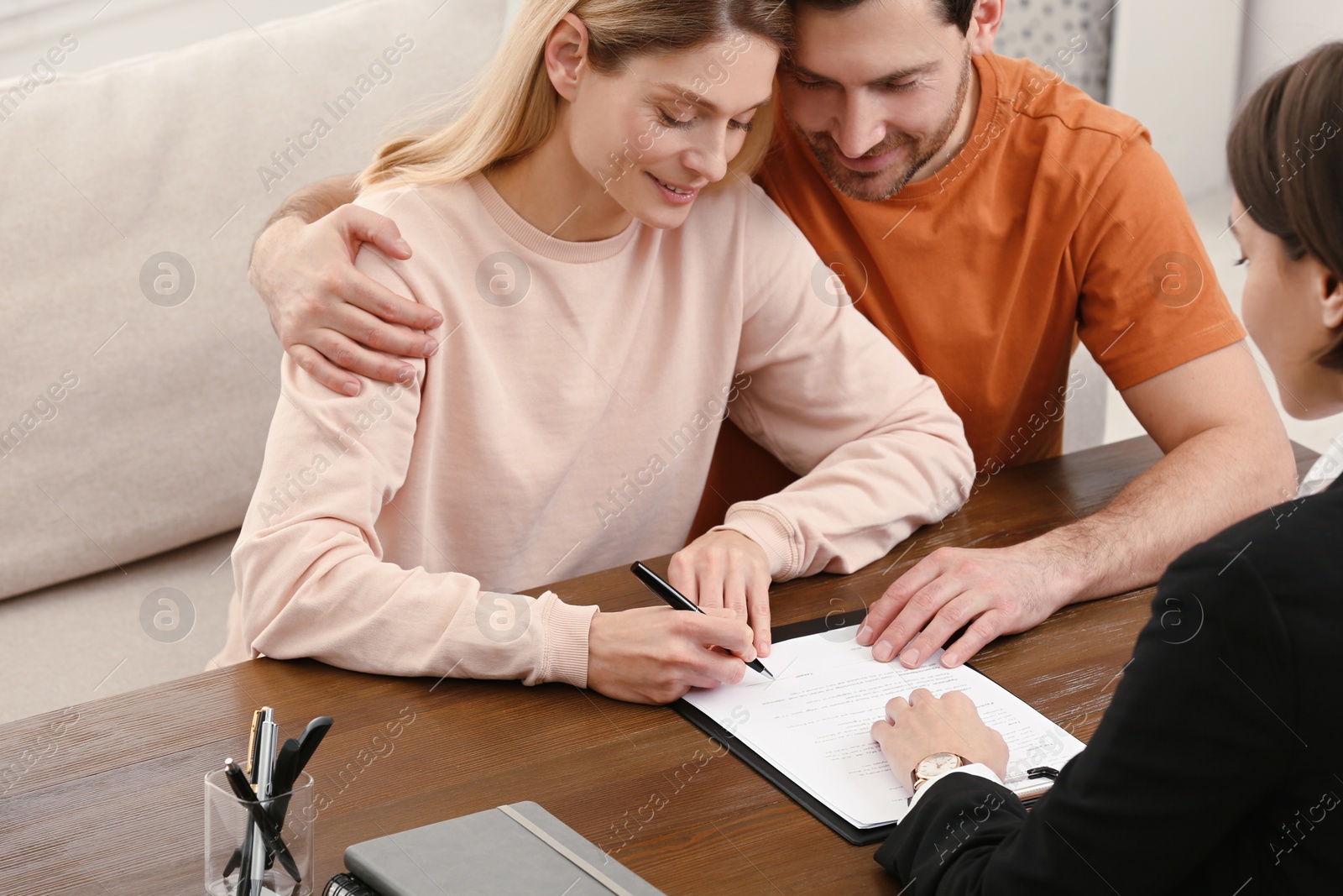 Photo of Notary helping couple with paperwork at wooden table, closeup