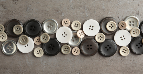 Many plastic sewing buttons on grey background, flat lay