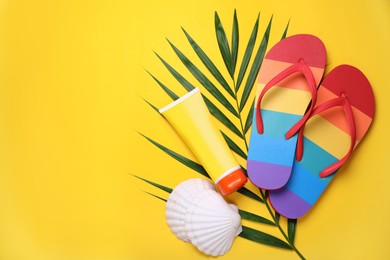 Photo of Rainbow flip flops, sunscreen, palm leaf and sea shells on yellow background, flat lay. Space for text