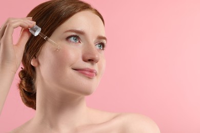 Photo of Beautiful woman with freckles applying cosmetic serum onto her face on pink background, closeup. Space for text