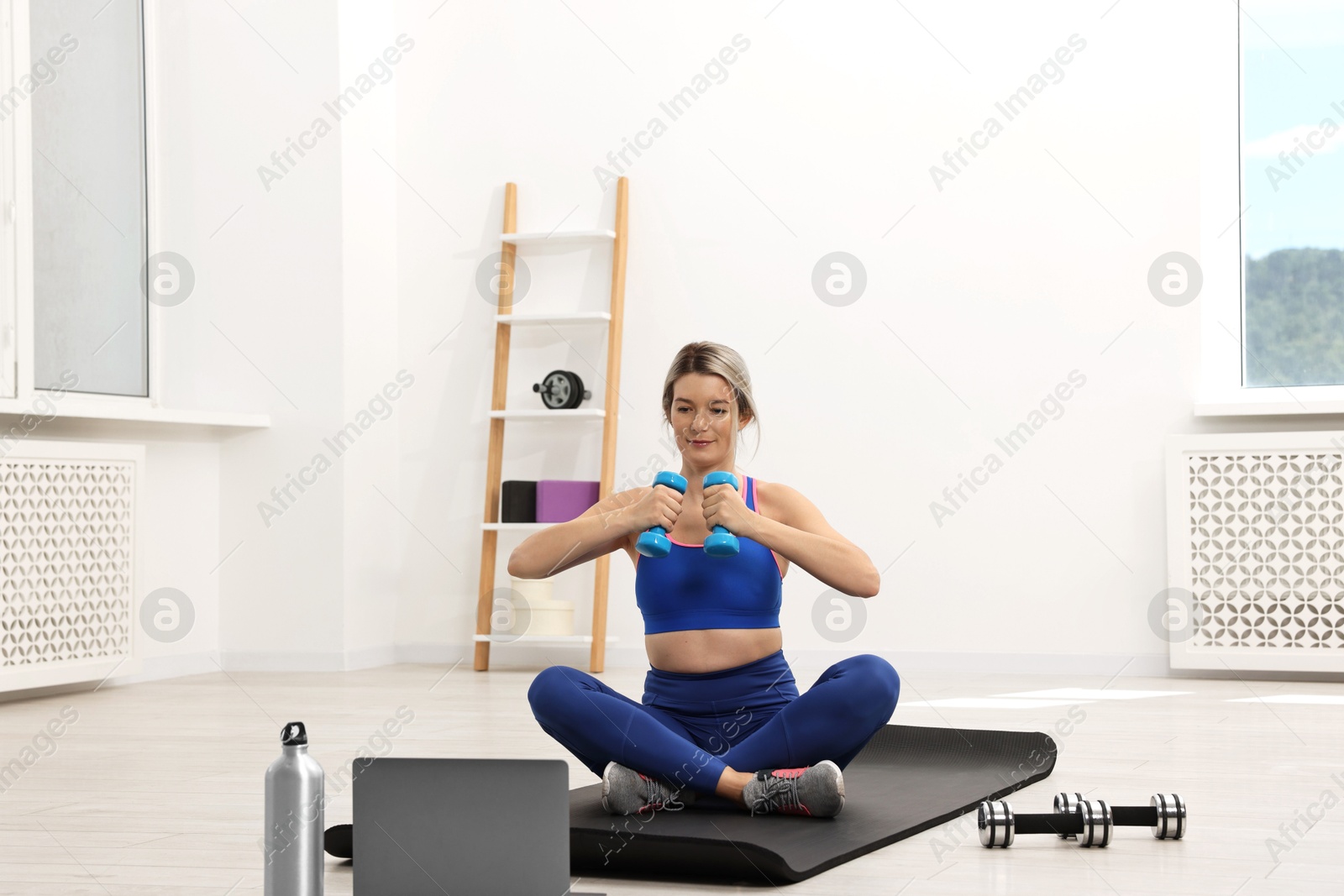 Photo of Online fitness trainer. Woman doing exercise with dumbbells near laptop at home