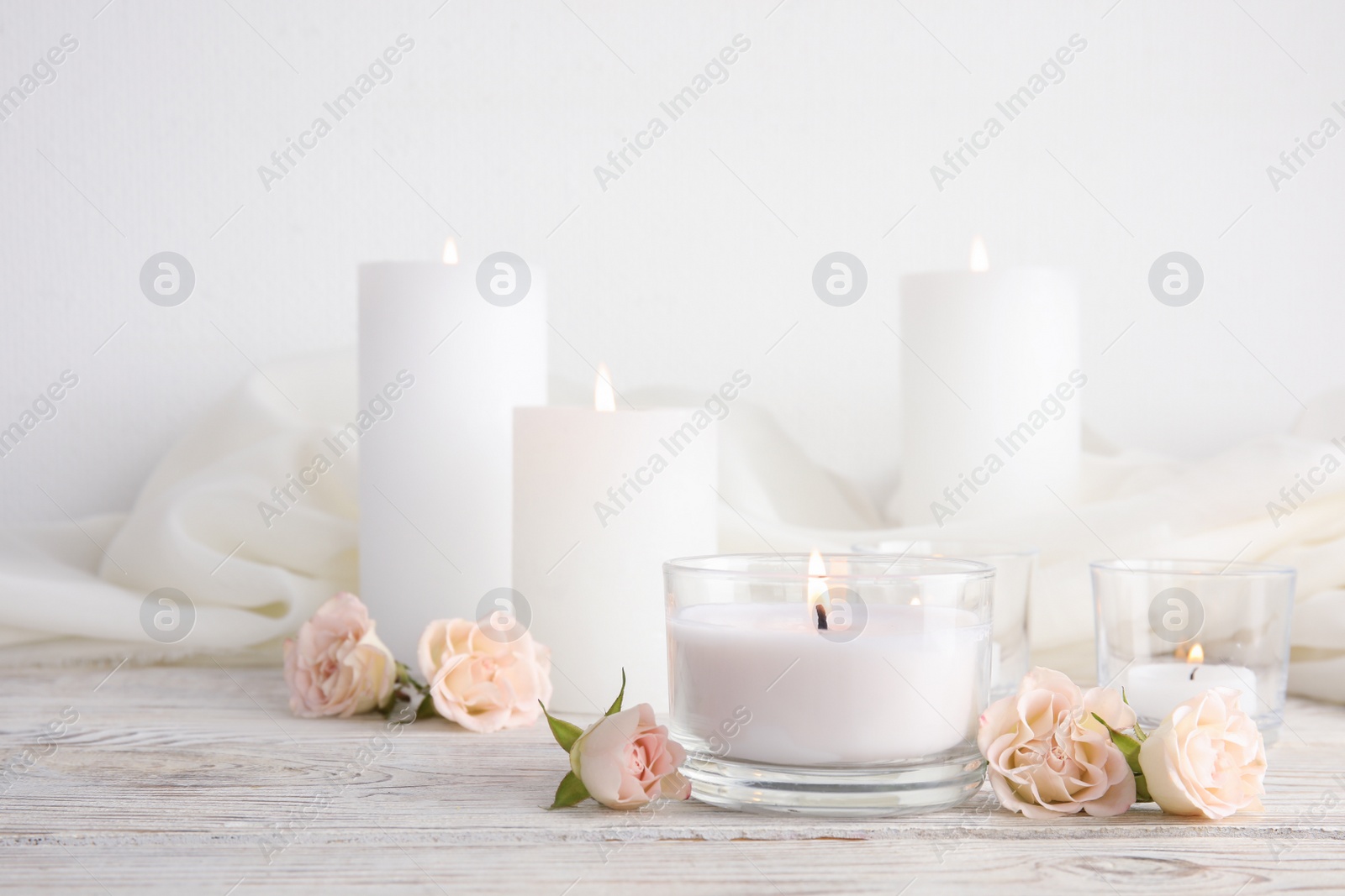 Photo of Composition with burning aromatic candles and roses on wooden table. Space for text