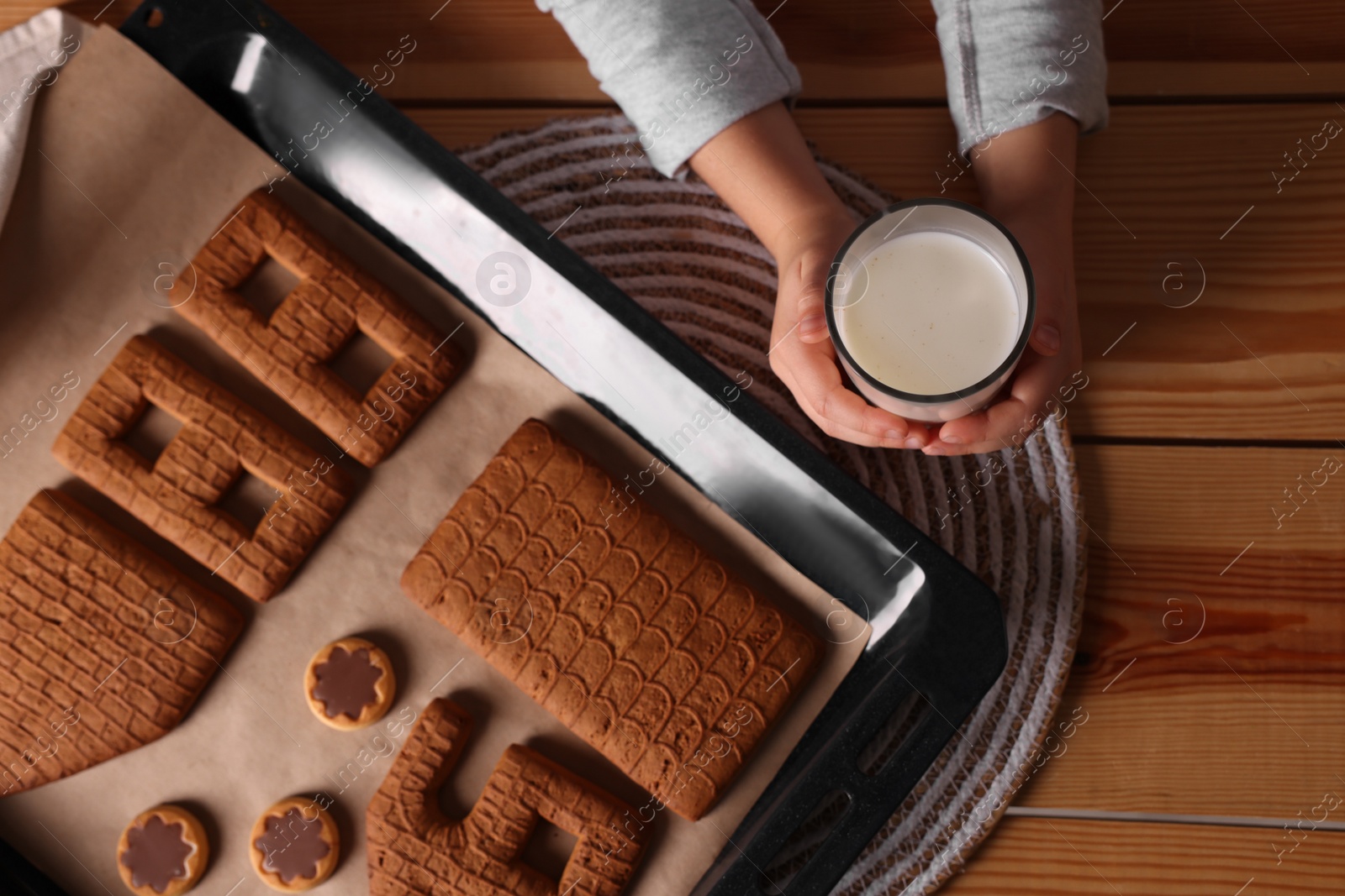 Photo of Little child holding glass of milk near baking sheet with Christmas pastry at wooden table, top view