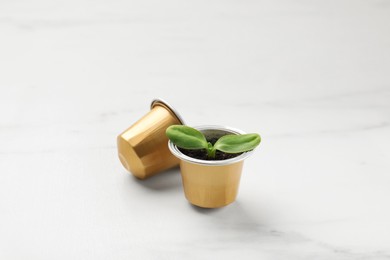 Photo of Coffee capsules and seedling on white marble table