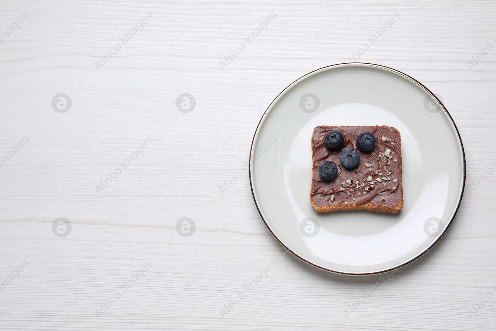 Photo of Toast with tasty nut butter, blueberries and nuts on white wooden table, top view. Space for text