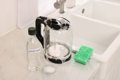 Photo of Cleaning electric kettle. Bottle of vinegar, sponge and baking soda on countertop in kitchen