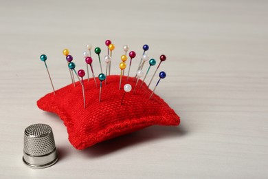 Pin cushion and thimble on white table. Space for text