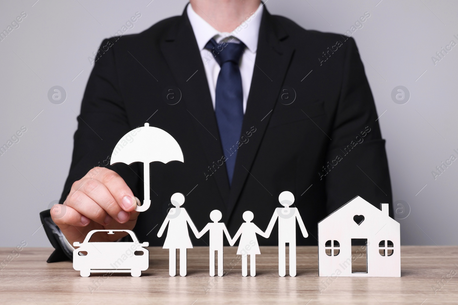 Photo of Man holding figure of umbrella near family, house and car at wooden table. closeup. Insurance concept