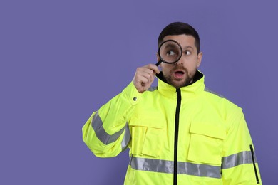 Surprised policeman looking through magnifier glass on violet background, space for text