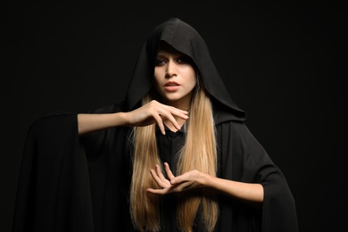 Photo of Witch in black mantle on dark background. Scary fantasy character