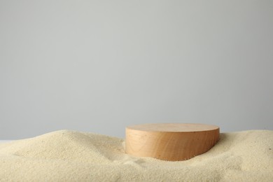 Presentation of product. Wooden podium on sand against grey background. Space for text