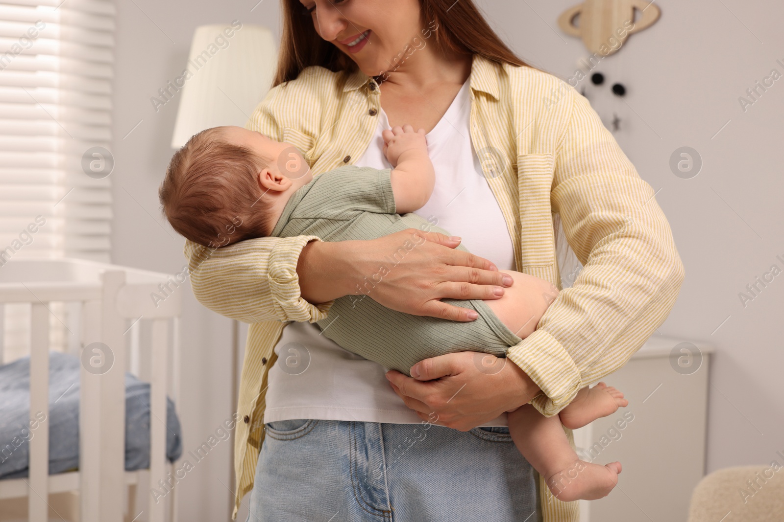 Photo of Mother holding her sleeping newborn baby in child`s room, closeup