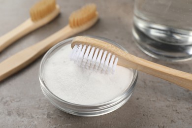 Photo of Bamboo toothbrushes and bowl of baking soda on grey table, closeup