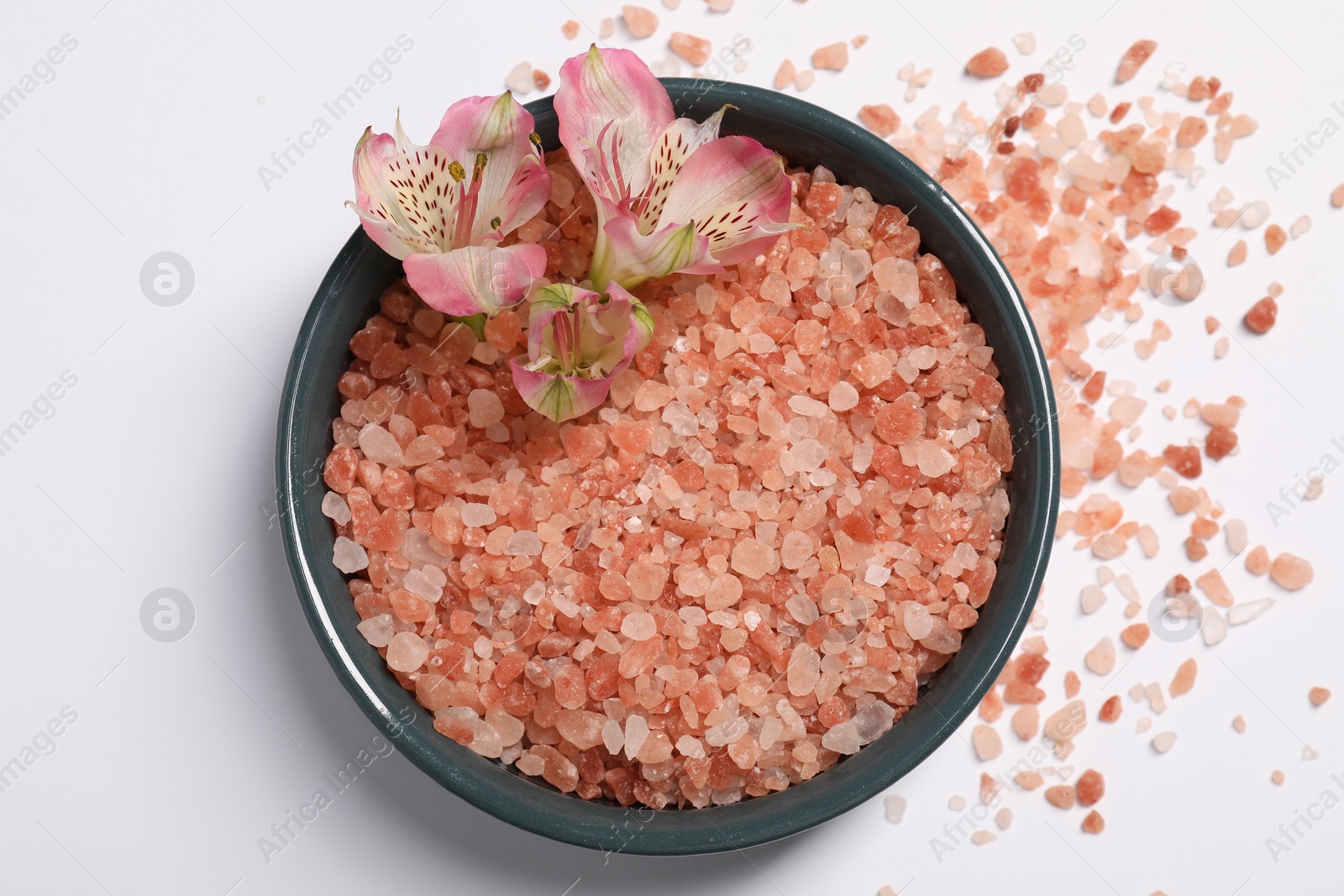 Photo of Natural sea salt and flowers in bowl on white background, top view