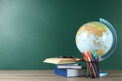 Photo of Globe, school supplies and magnifying glass on wooden table near green chalkboard, space for text. Geography lesson