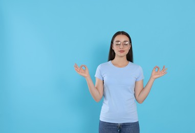 Photo of Find zen. Beautiful young woman meditating on light blue background. Space for text