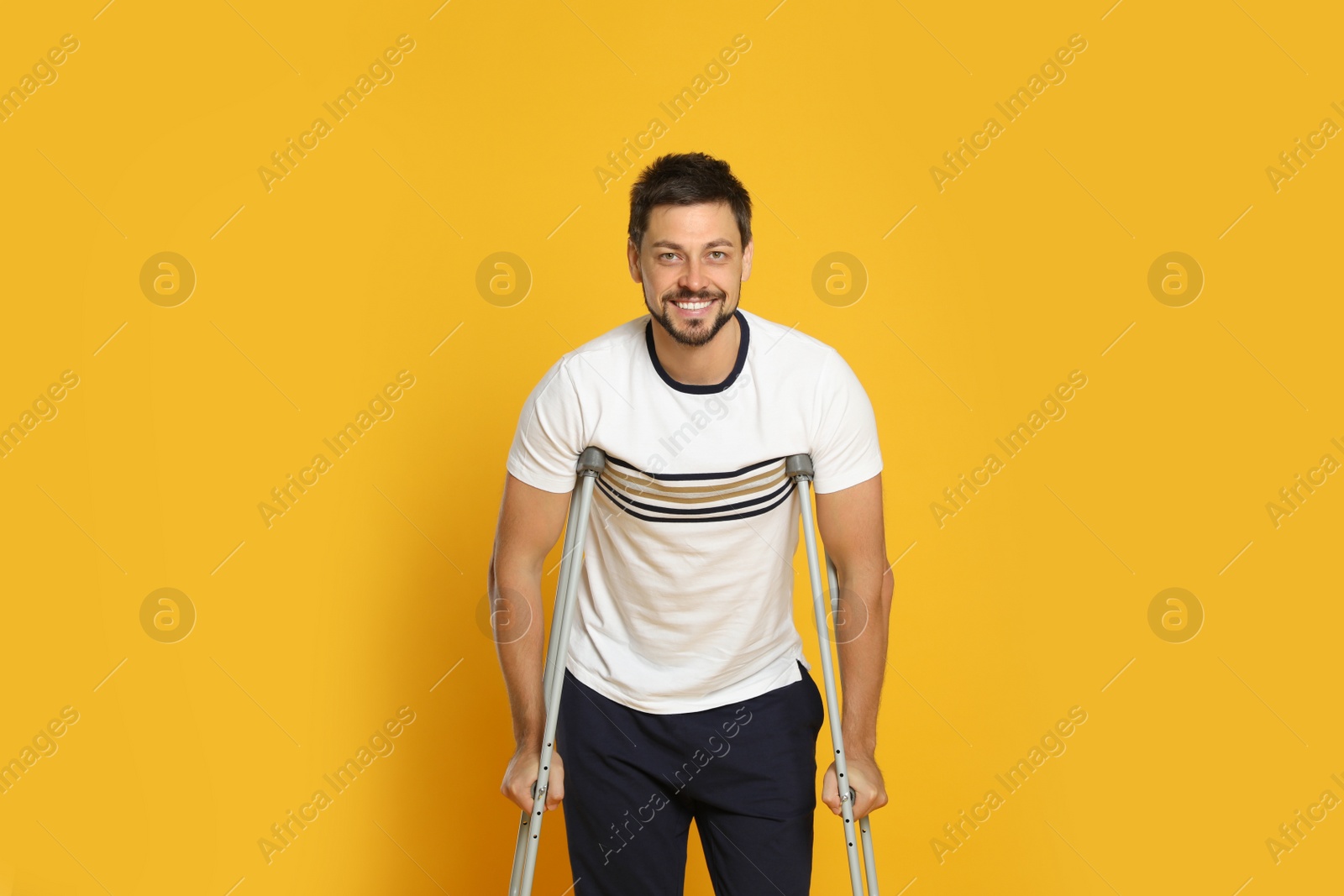 Photo of Portrait of happy man with crutches on yellow background