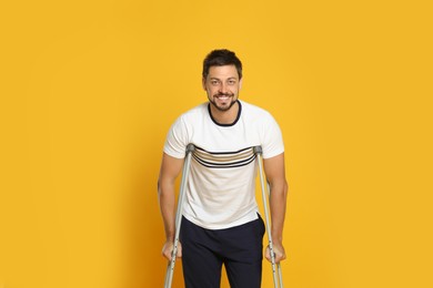 Photo of Portrait of happy man with crutches on yellow background