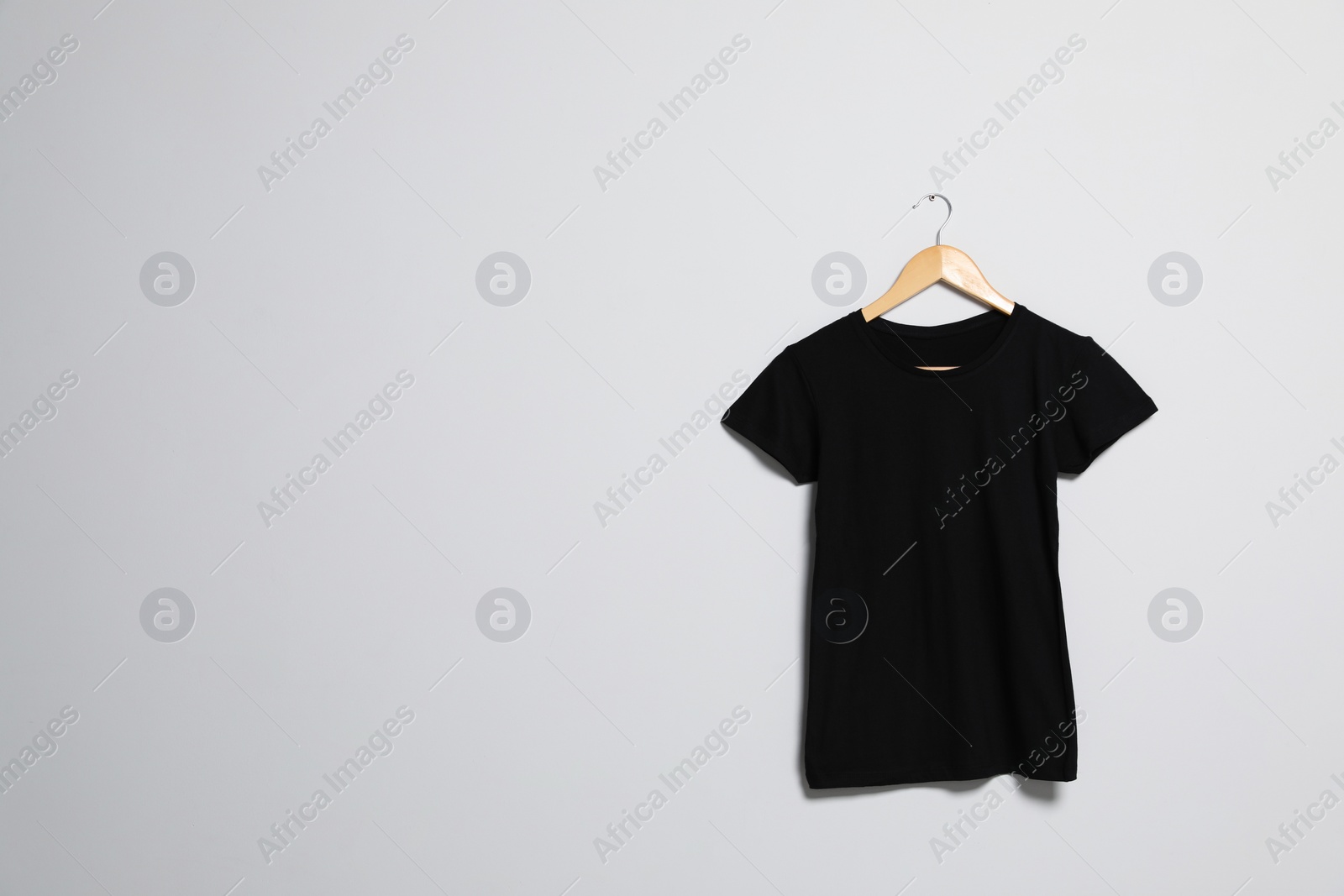 Photo of Hanger with black t-shirt on light wall. Mockup for design