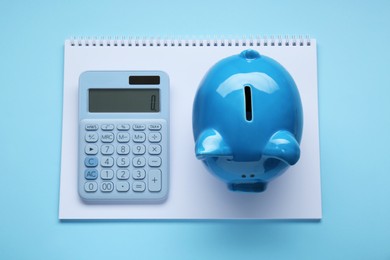 Photo of Piggy bank, notebook and calculator on light blue background, top view