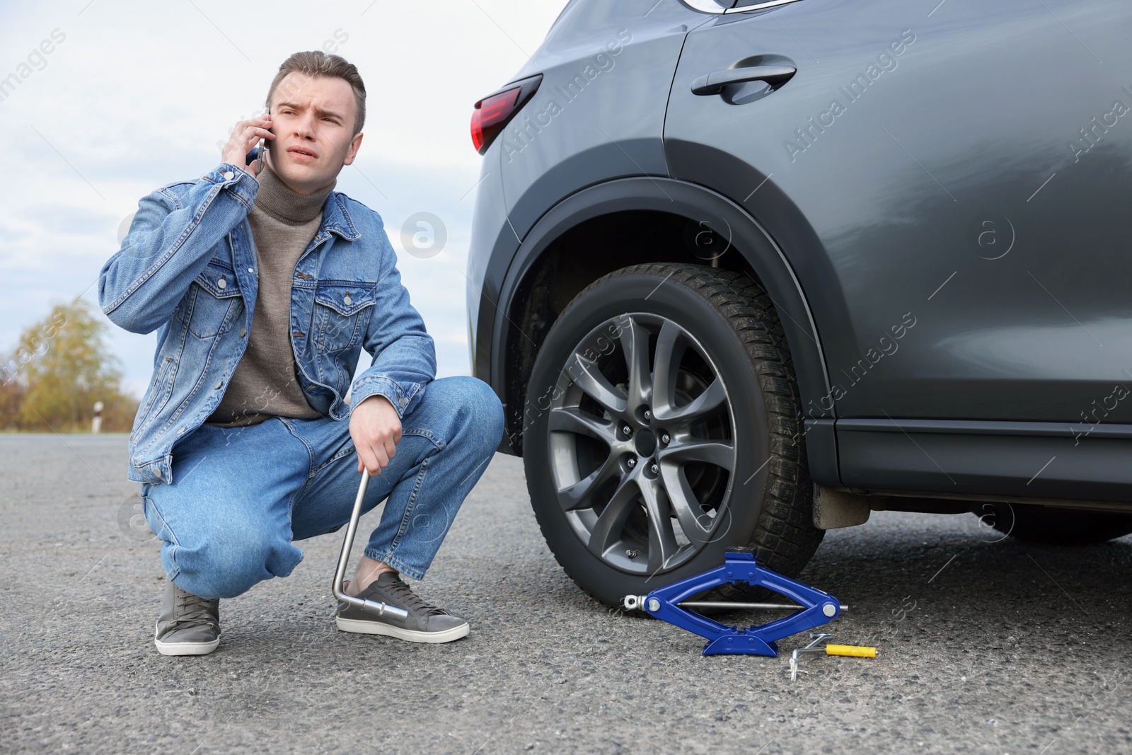 Photo of Worried young man calling car service. Tire puncture