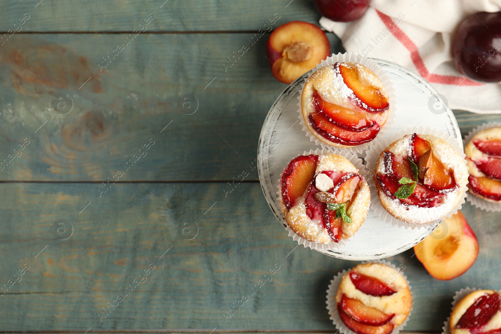 Photo of Delicious sweet cupcakes with plums on wooden table, flat lay. Space for text