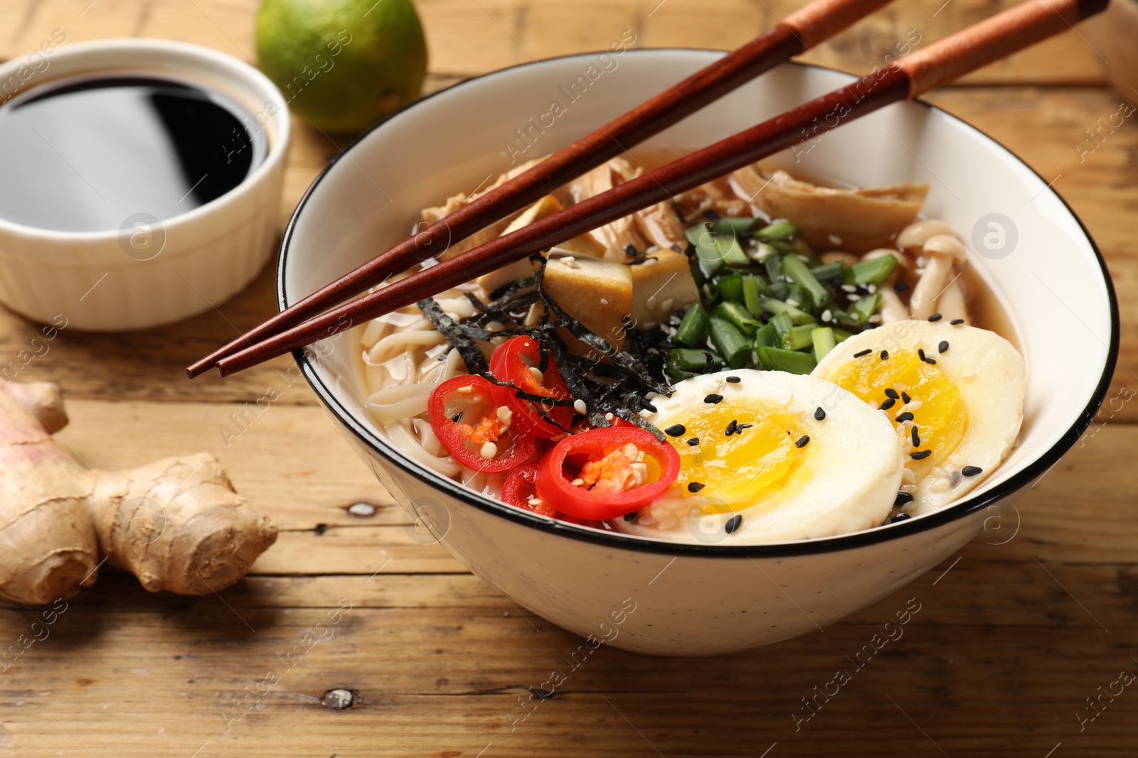 Photo of Bowl of delicious ramen and chopsticks on wooden table, closeup. Noodle soup