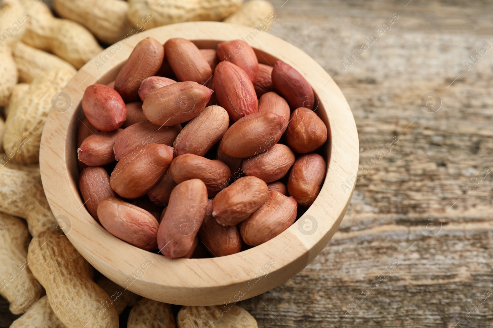 Photo of Fresh unpeeled peanuts in bowl on wooden table, closeup