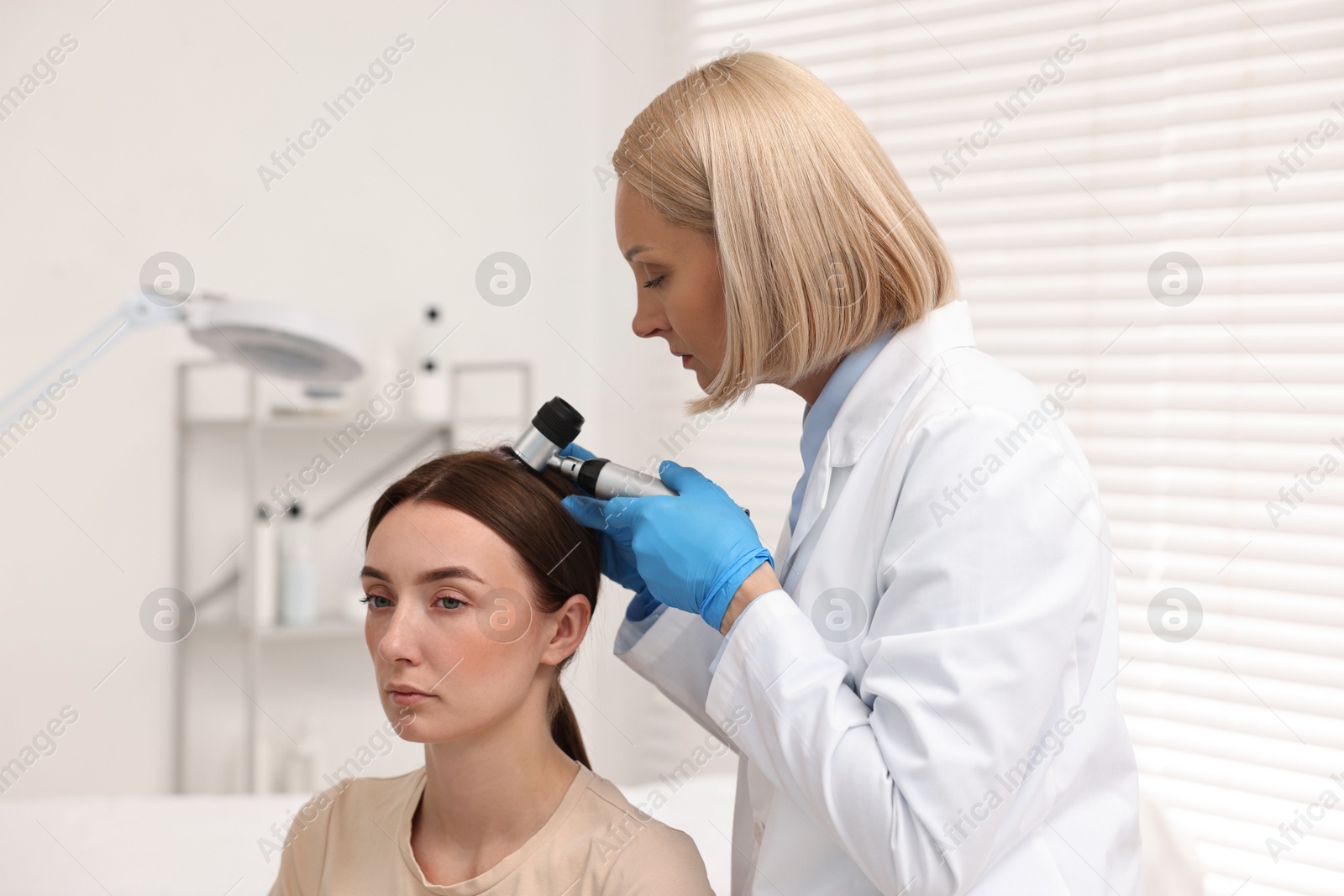 Photo of Trichologist with dermatoscope examining patient`s hair in clinic