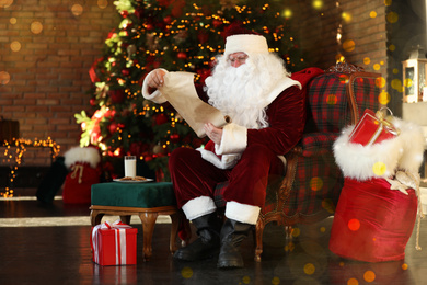 Photo of Santa Claus with wish list near Christmas tree indoors