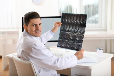 Orthopedist examining X-ray picture at desk in clinic