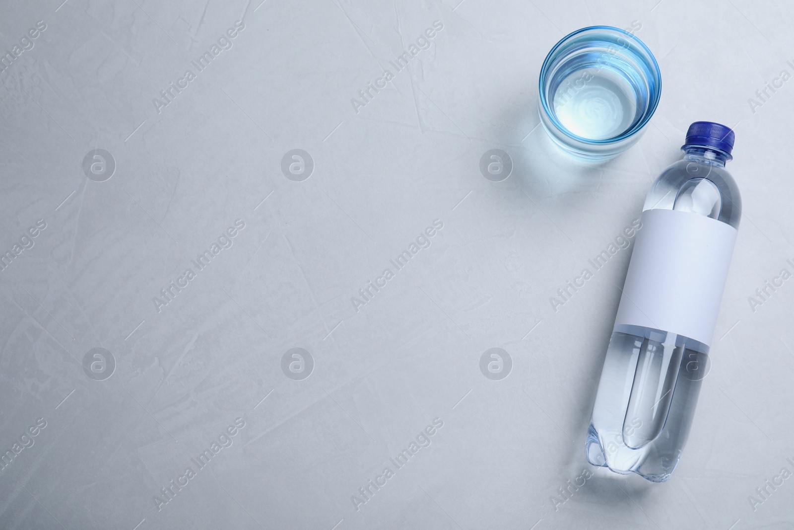 Photo of Plastic bottle and glass with water on grey table, flat lay. Space for text