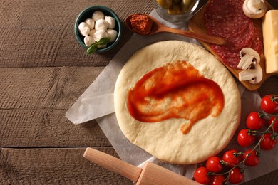Photo of Pizza dough with tomato sauce, products and rolling pin on wooden table, flat lay. Space for text