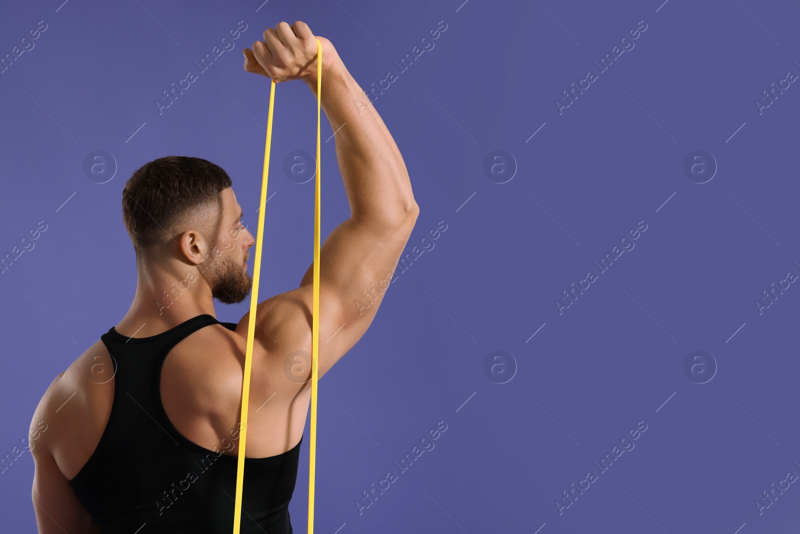 Photo of Muscular man exercising with elastic resistance band on purple background, back view. Space for text