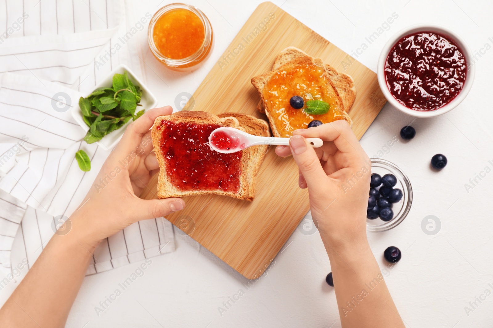 Photo of Woman spreading sweet jam on toast over table, top view