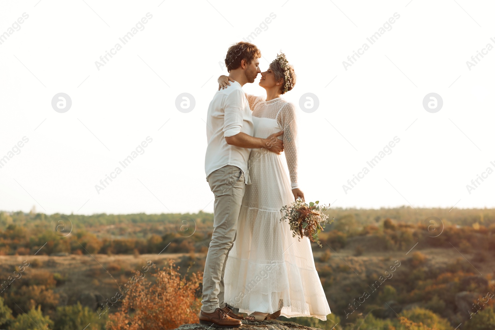 Photo of Happy newlyweds with beautiful field bouquet outdoors