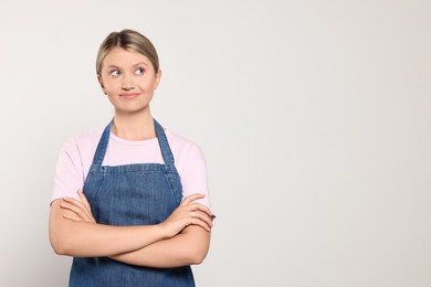 Beautiful young woman in denim apron on light grey background. Space for text