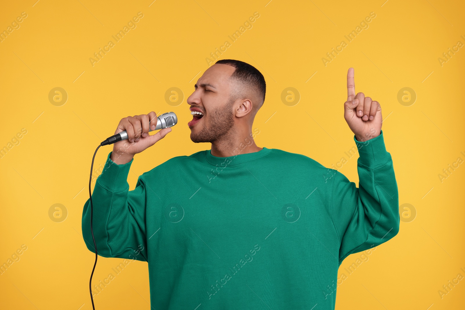 Photo of Handsome man with microphone singing on orange background