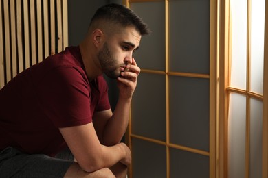 Photo of Sad young man at home. Space for text