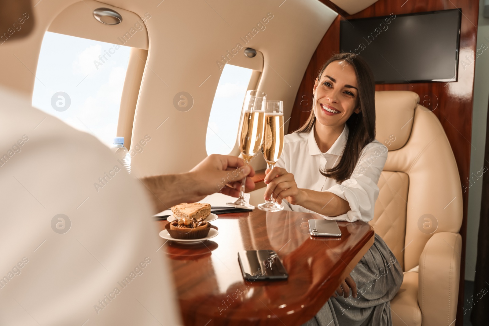 Photo of Colleagues clinking glasses of champagne at table in airplane during flight