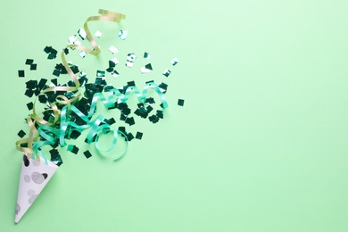 Photo of Shiny confetti and streamers with party cracker on light green background, top view. Space for text