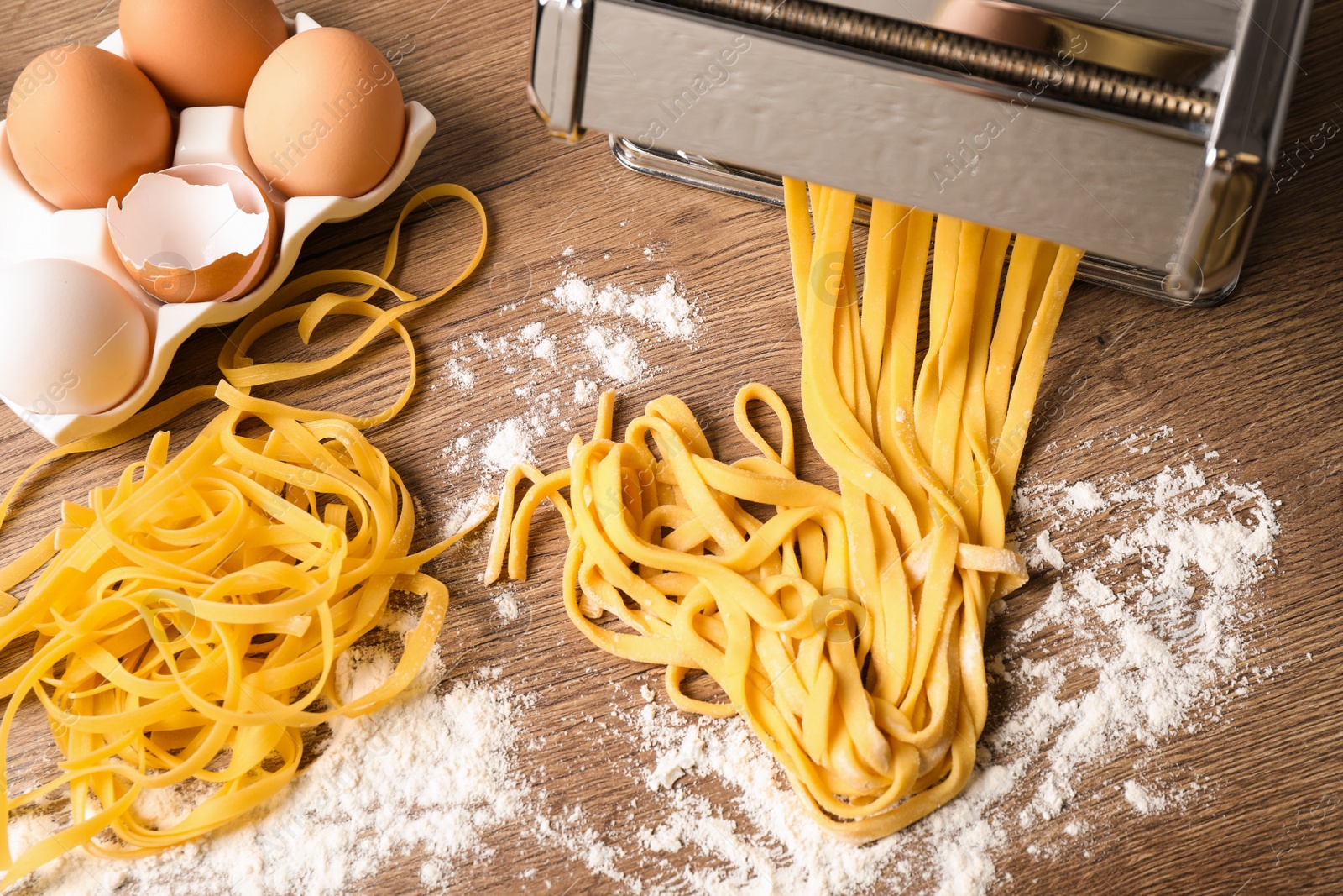 Photo of Pasta maker machine with dough and products on wooden table, flat lay